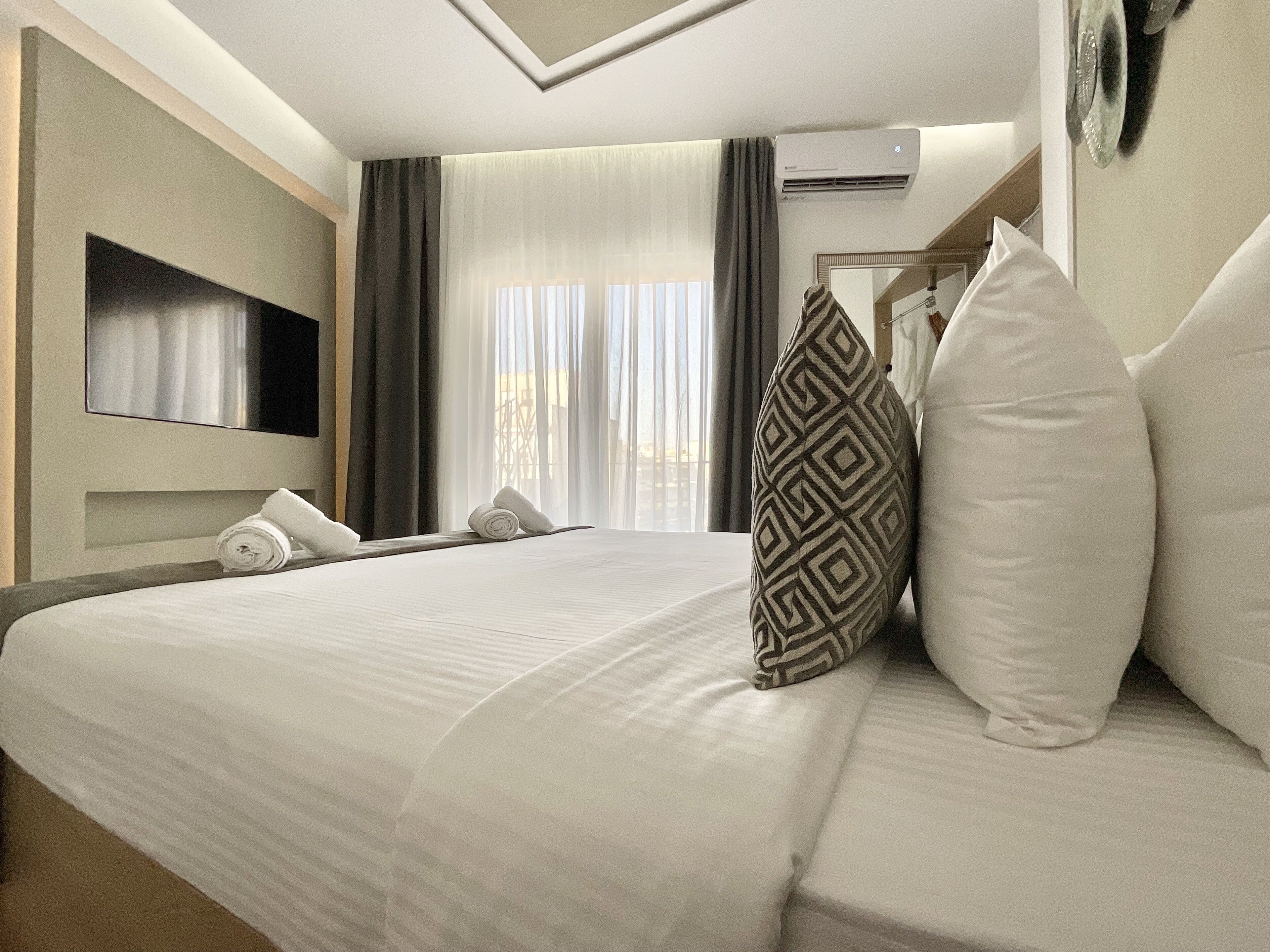 A hotel room with a large bed, a flat-screen TV mounted on the wall, and an air conditioning unit.