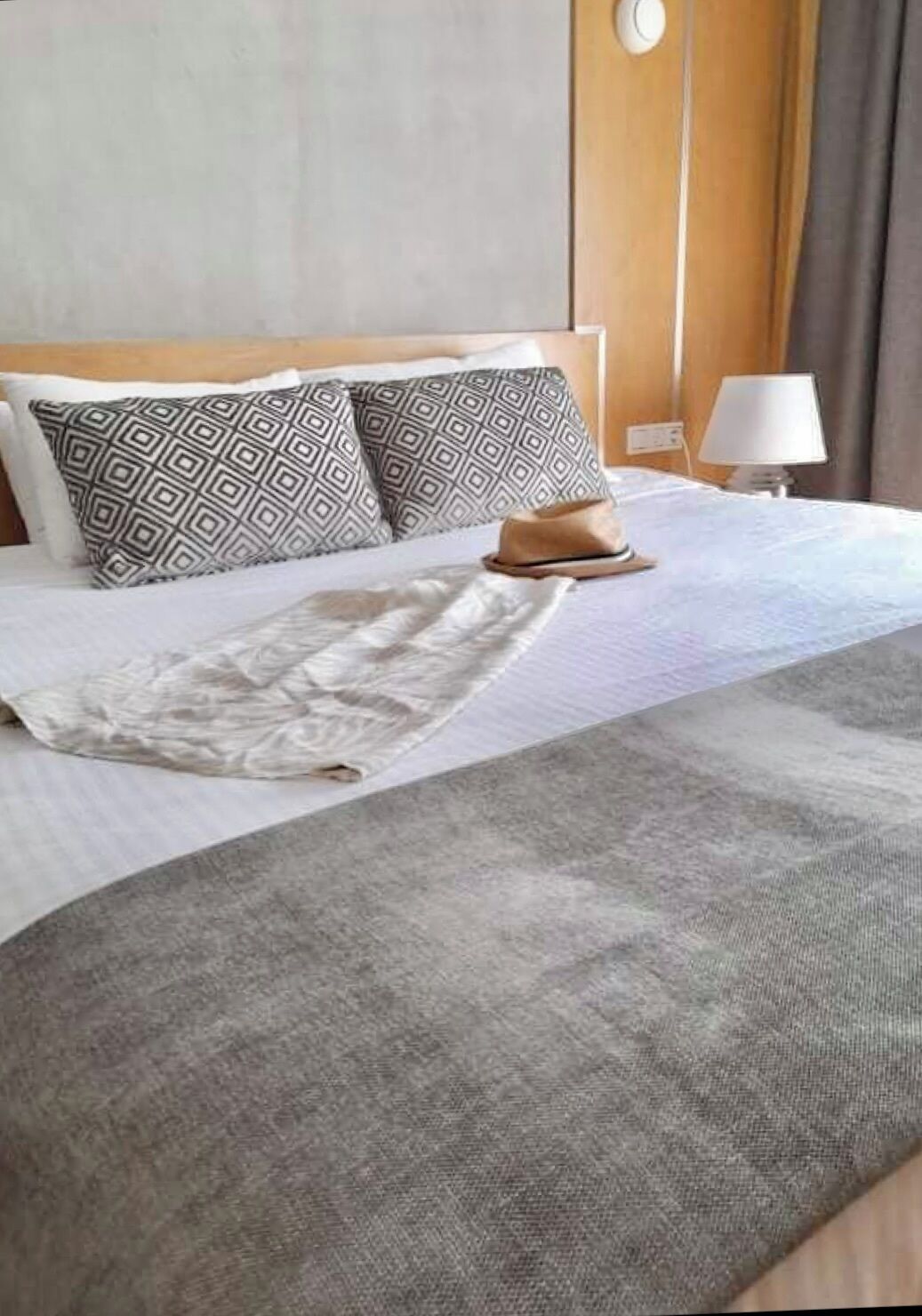 Ein ordentlich gemachtes Bett mit gemusterten Kissen, einem Hut und einer Decke.