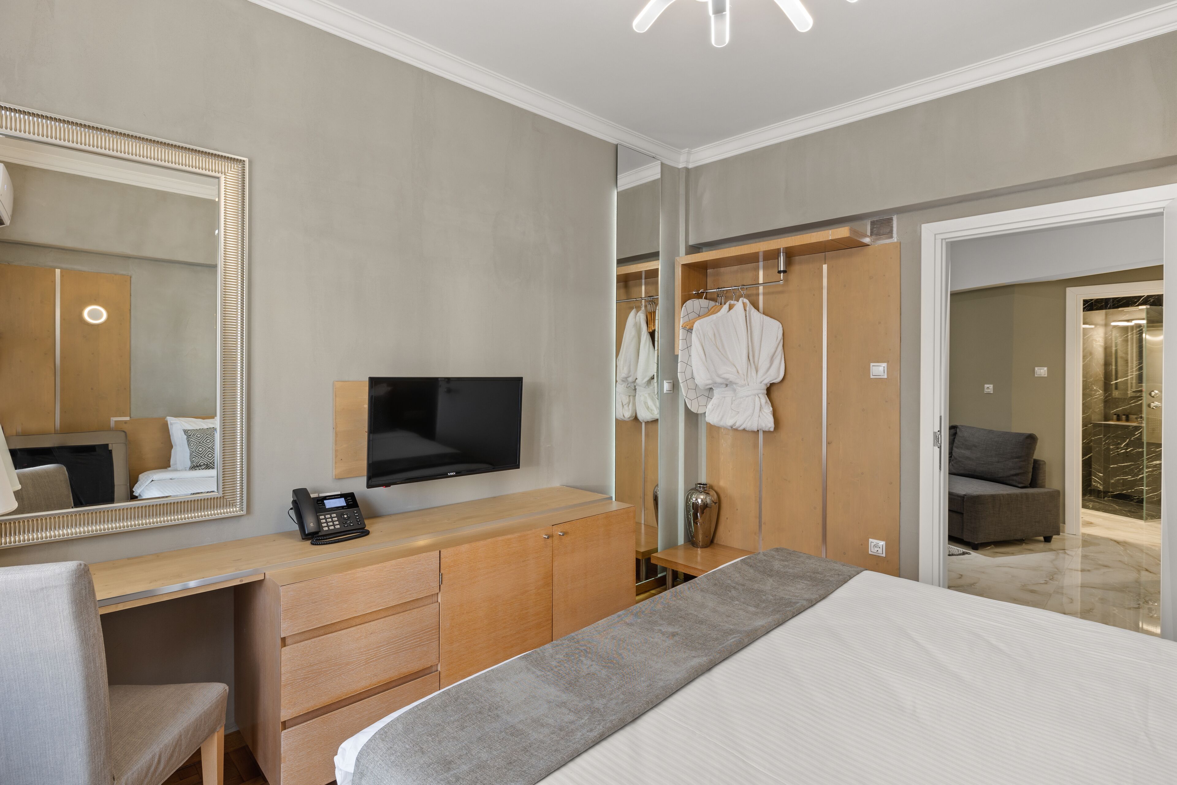 Una camera d'albergo moderna con un letto grande, una scrivania con televisione a schermo piatto, uno specchio e un armadio a muro con accappatoi.