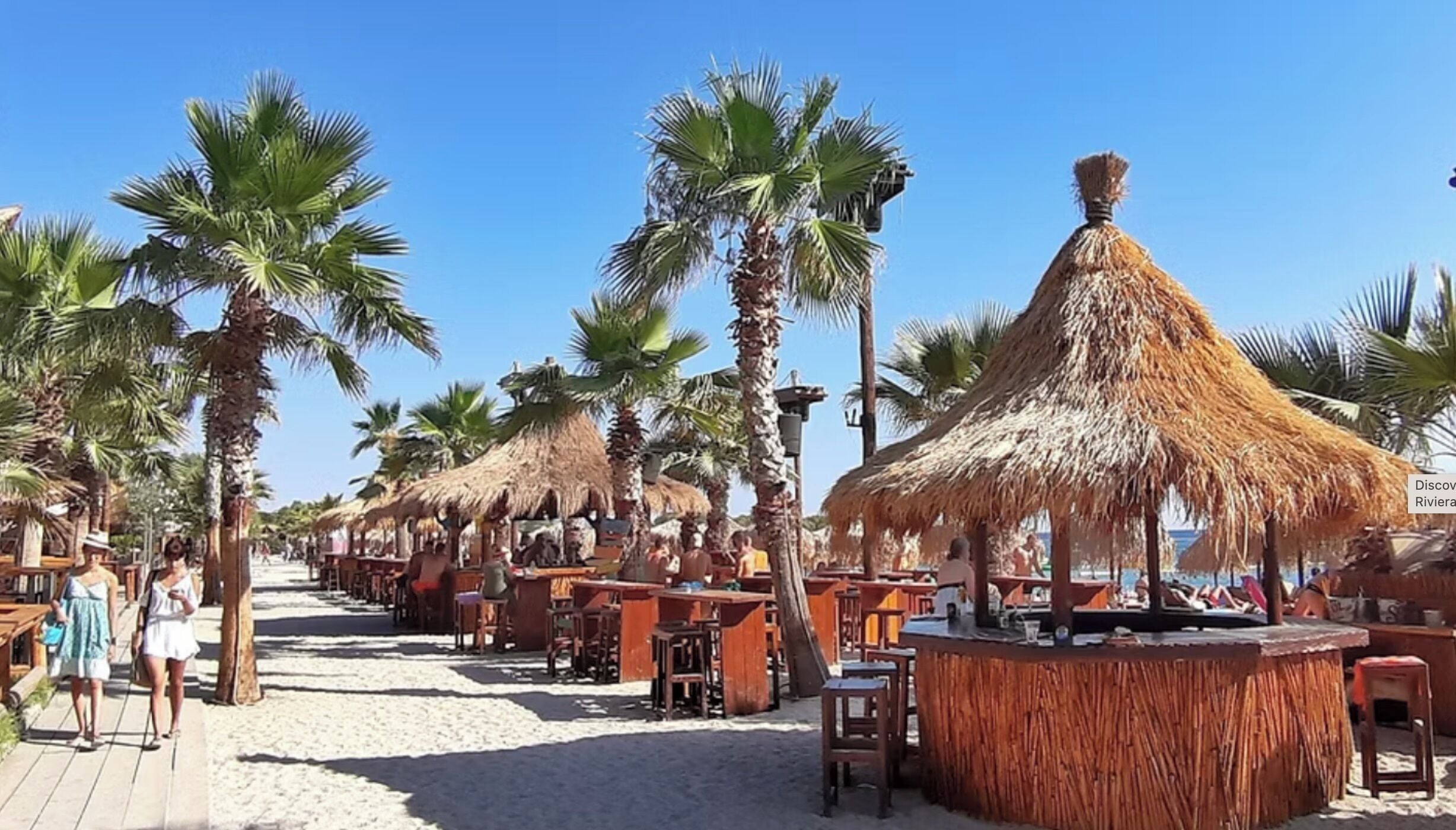 A beachside restaurant with thatched umbrellas and wooden tables.