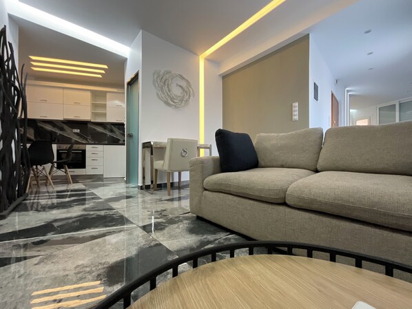 A modern living room with a sofa, a dining table, and a kitchen area in the background.