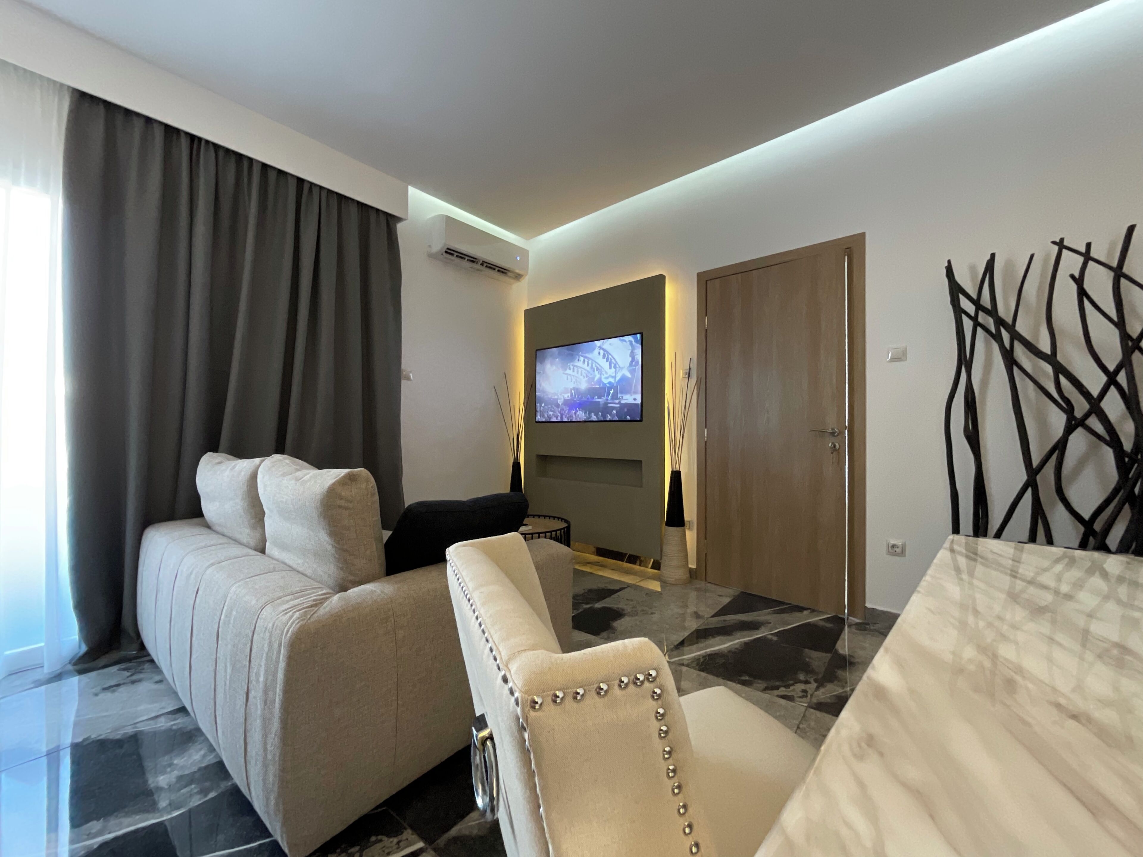 Una habitación de hotel moderna con sofá, una mesa de comedor, un televisor montado en la pared y un elemento decorativo en la pared.