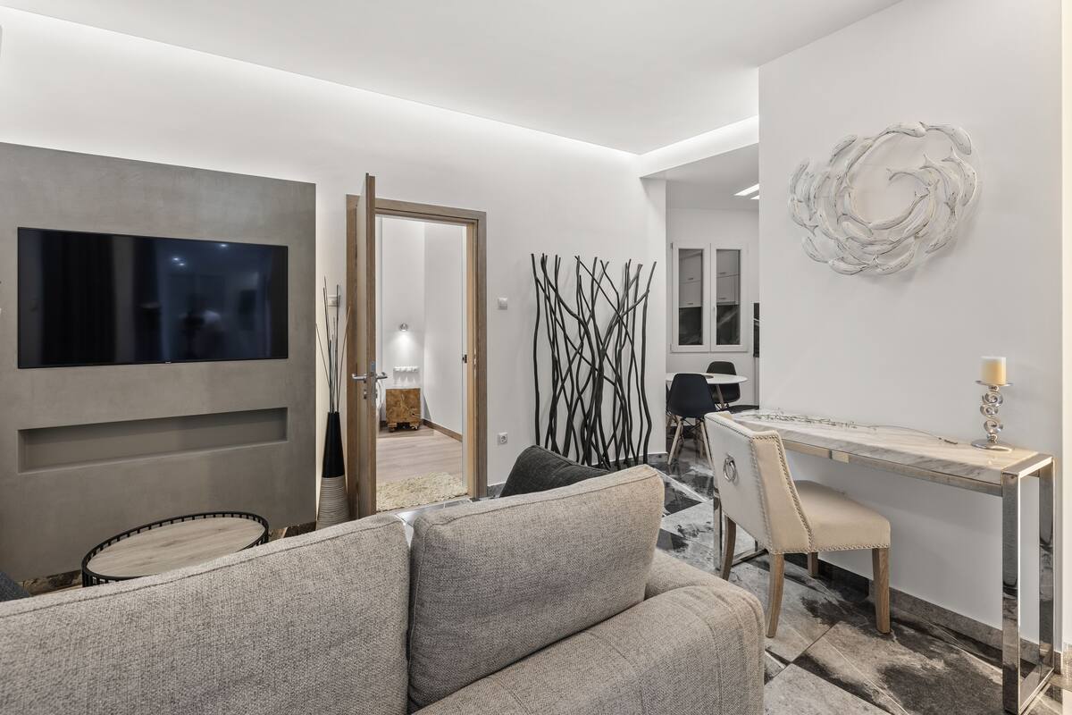 Un salon moderne avec un canapé gris, un téléviseur à écran plat, un coin repas doté d’une table en marbre et un élément décoratif mural.