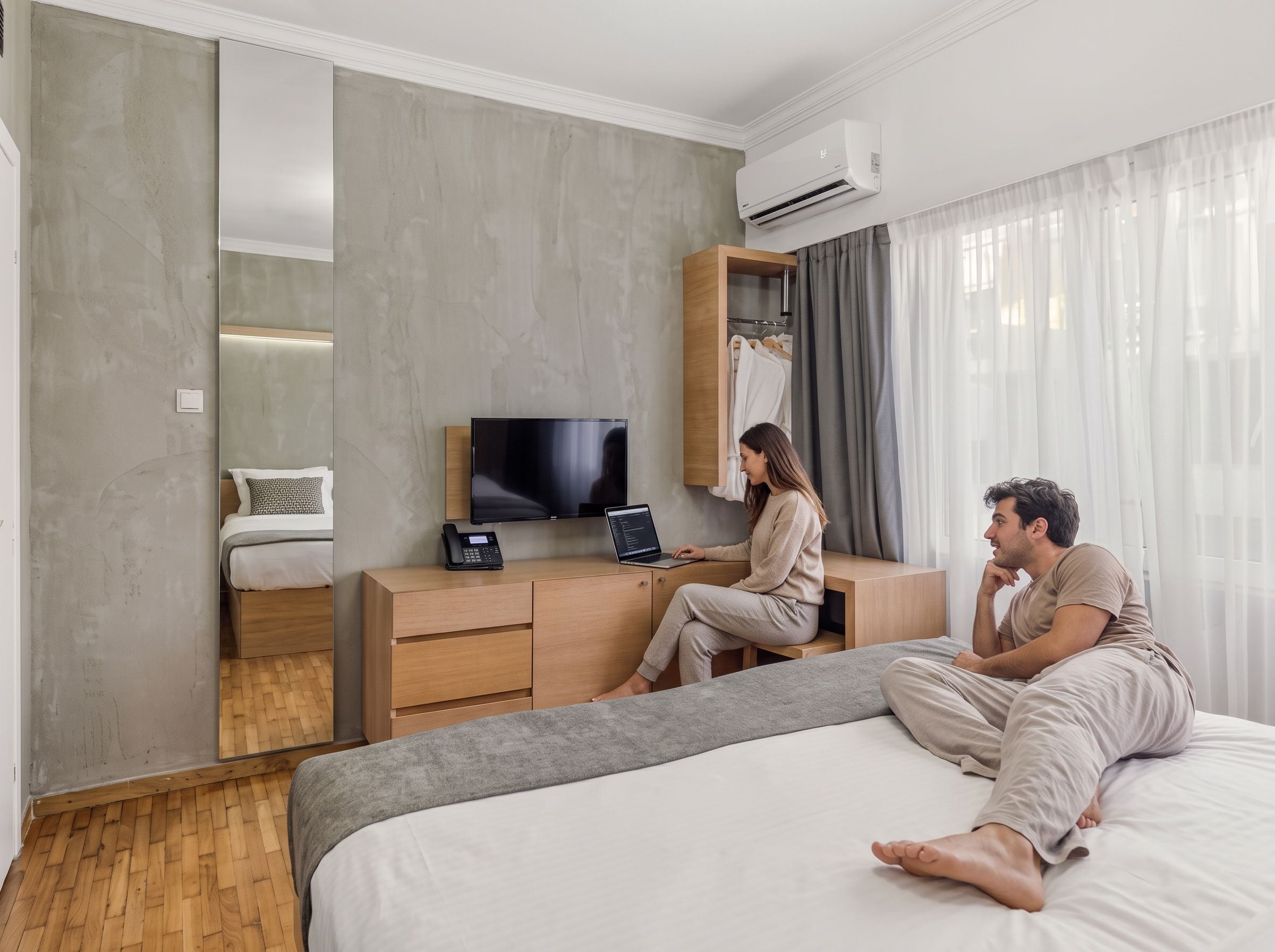 Hotellihuone, jossa on sänky, työpöytä, jossa on kannettava tietokone ja puhelin, televisio ja vaatekaappi.