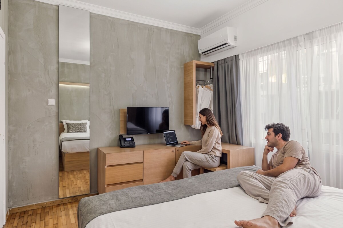 Habitación de hotel con cama, escritorio, computadora portátil, teléfono, televisión y armario.
