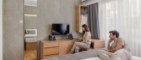 Hotellihuone, jossa on sänky, työpöytä, jossa on kannettava tietokone ja puhelin, televisio ja vaatekaappi.