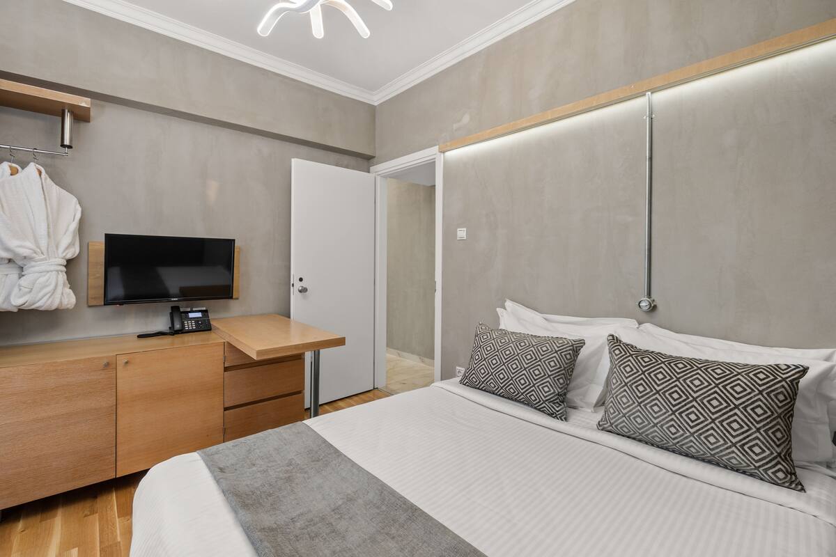 Une chambre d’hôtel moderne, équipée d’un lit, d’un bureau avec un téléphone, d’une télévision et d’un peignoir accroché au mur.