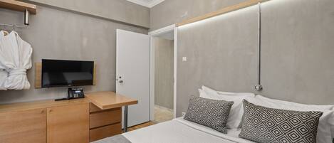 Quarto de hotel moderno com uma cama, uma escrivaninha com telefone, televisão e um roupão pendurado na parede.
