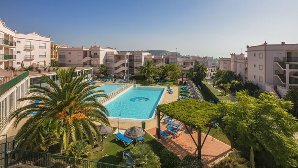 Ein Resort mit einem zentral gelegenen Swimmingpool, umgeben von Liegestühlen und Palmen.