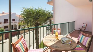 Ein Balkon mit einem runden Holztisch, zwei gepolsterten Stühlen, einer Weinflasche und einem Buch.