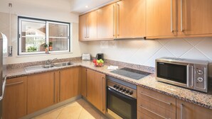 Eine moderne Küche mit Holzausstattung, Backofen, Mikrowelle und einem Fenster mit Blick auf ein Haus und Grünflächen.