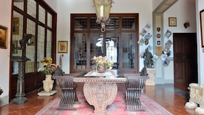 A traditional room with a wooden ceiling, a large window with a view, a table with a vase of flowers, and a wall with various decorations.