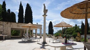 An outdoor patio area with stone flooring, lounge chairs, and thatched umbrellas.