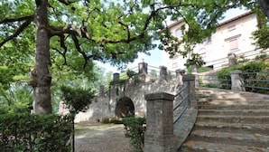 A stone staircase leading up to a stone bridge with a metal railing, surrounded by trees and greenery.
