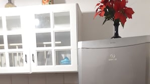 Eine Küche mit einem Edelstahl-Kühlschrank, einem hölzernen Hocker, einer Toilettenpapierrolle und weißen Schränken mit Glastüren.