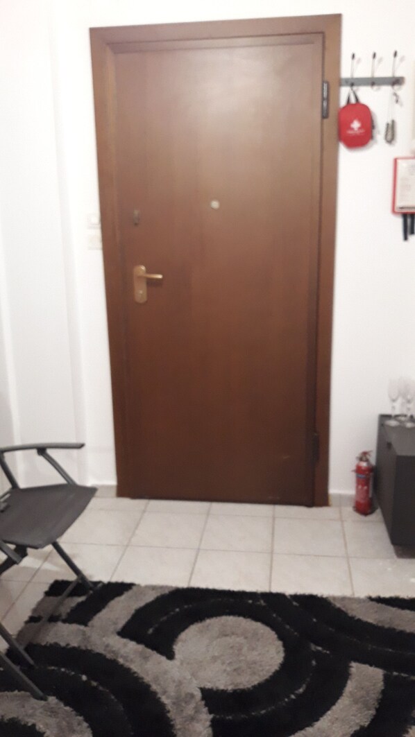 A closed wooden door with a brass handle, a black folding chair, a patterned rug, a red bag hanging on a hook, and a fire extinguisher on the floor.