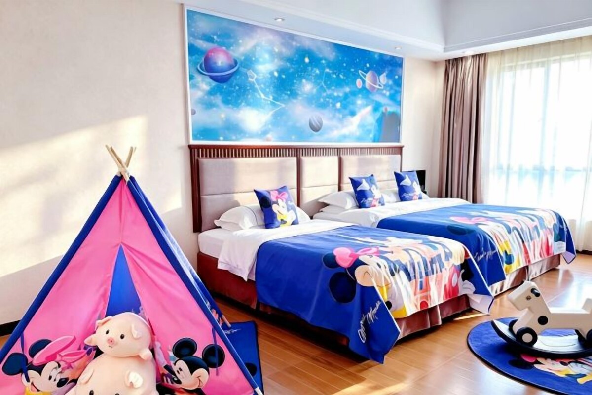 Ein Hotelzimmer mit zwei Betten, einem großen Fenster, einem Wandgemälde zum Thema Weltraum und einer Spielzone im Mickey-Mouse-Design.