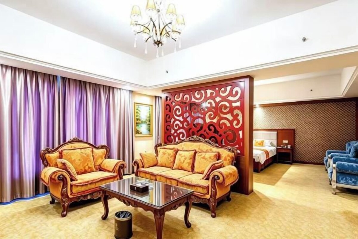 Ein Hotelzimmer mit einer Sofagarnitur, einem Bett, einem blauen Sessel und einer dekorativen Wandverkleidung.