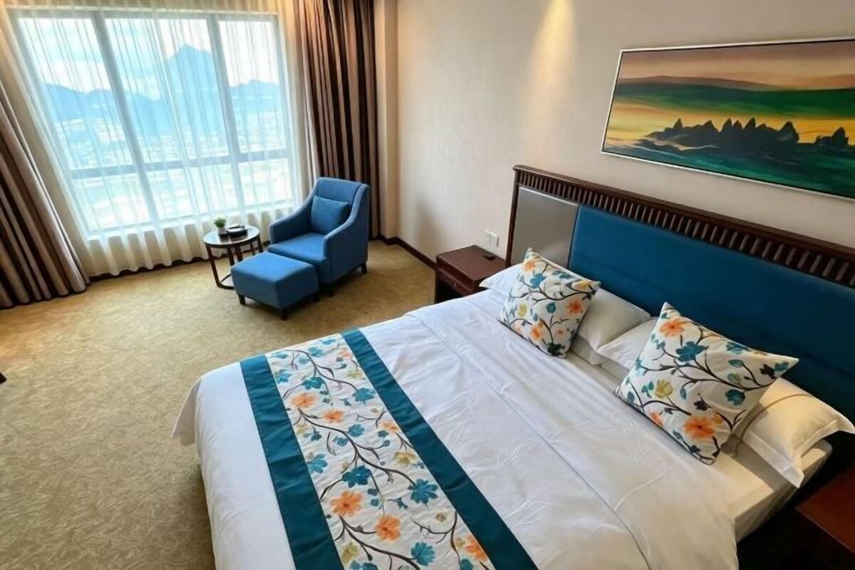 Ein Hotelzimmer mit einem großen Bett, einem blauen Sessel, einem kleinen Tisch und einem Bild an der Wand.