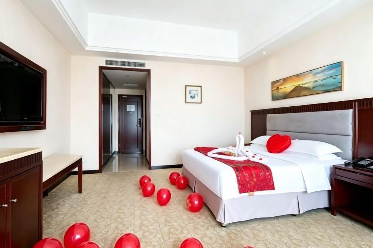 Ein Hotelzimmer mit einem Bett, einem Fernseher, einem Schreibtisch und einer Tür zu einem weiteren Raum.