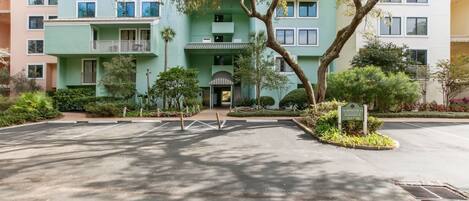 A multi-story residential building with balconies, a gated entrance, and surrounding greenery.