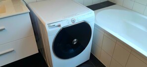 A front-loading washing machine next to a bathtub in a bathroom. - Ferienhaus Kleine Weite Welt (Nümbrecht)