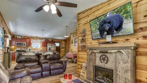 L’intérieur d’un chalet est aménagé avec une cheminée, un canapé en cuir et un téléviseur fixé au mur.