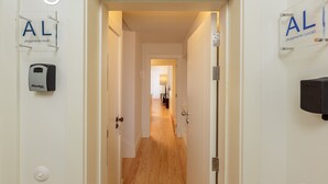 A hallway with a wooden floor, a door with a handle, and a wall-mounted dispenser. - YOUROPO - Flores (Porto)