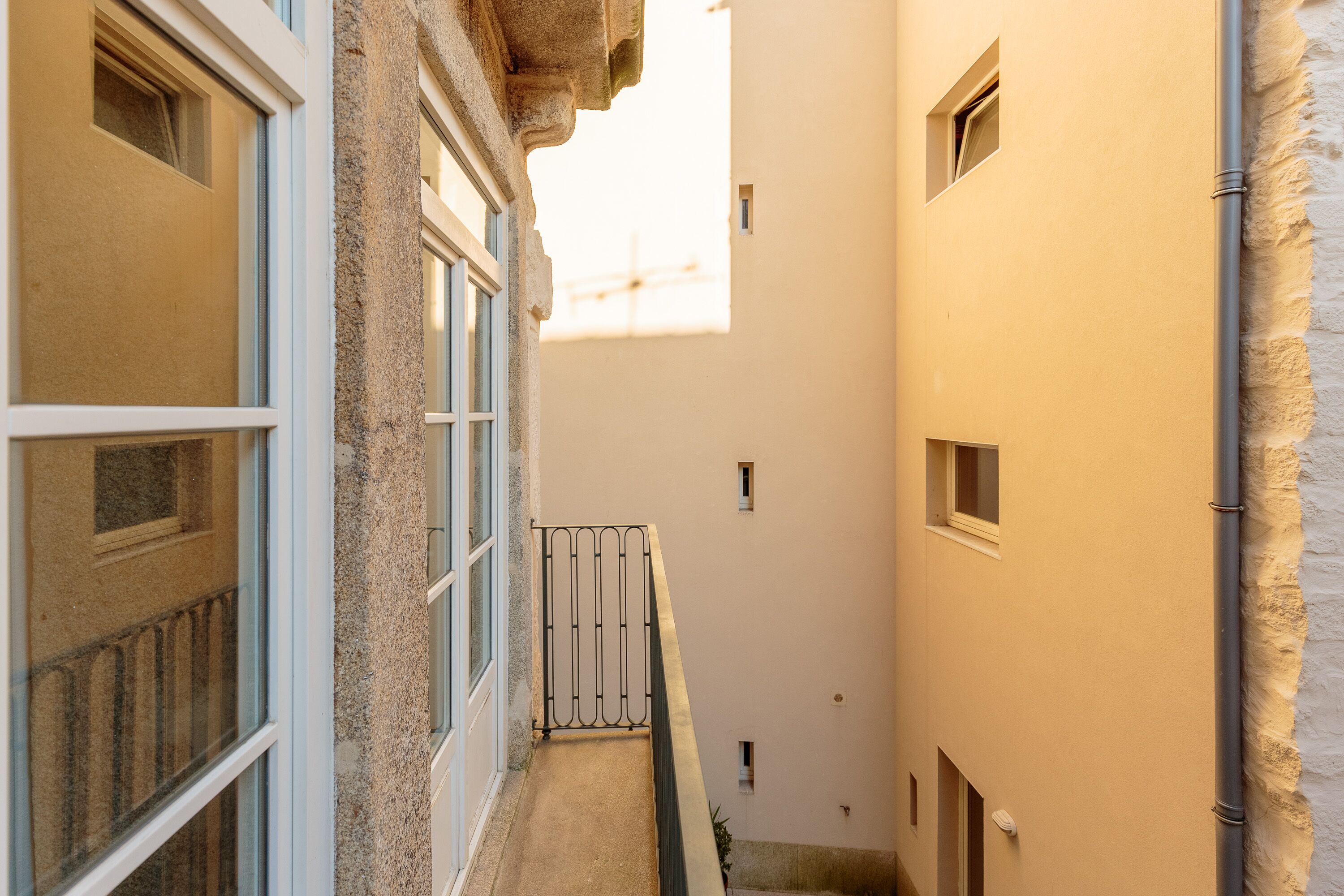 Ein schmaler Gang mit Gebäuden an beiden Seiten, mit einem kleinen Balkon mit Metallgeländer und einem Fenster.