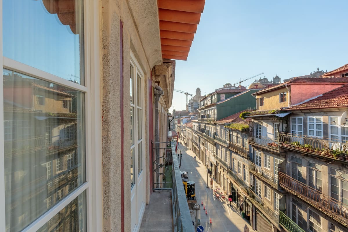 A narrow street with buildings on both sides, balconies with railings, and a clear sky.