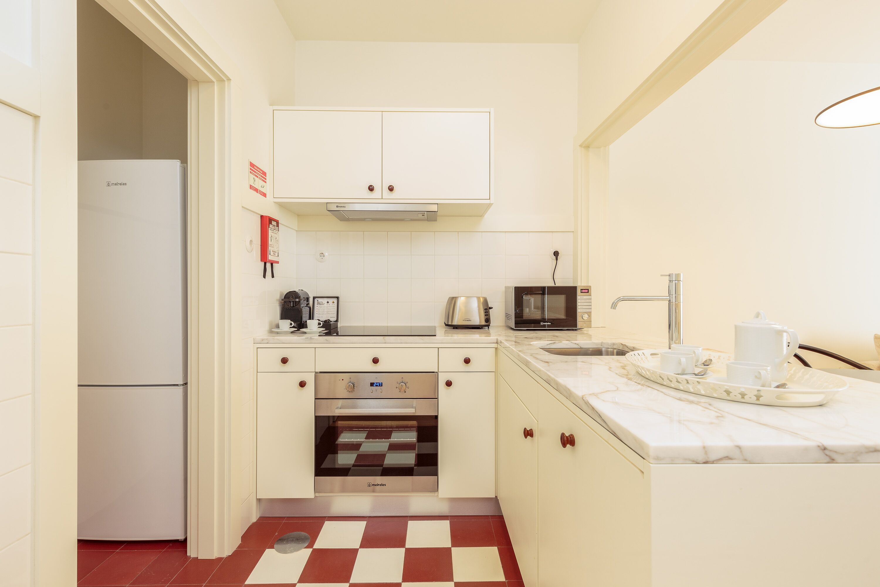 A compact kitchen with white cabinets, a built-in oven, a microwave, a toaster, and a sink.