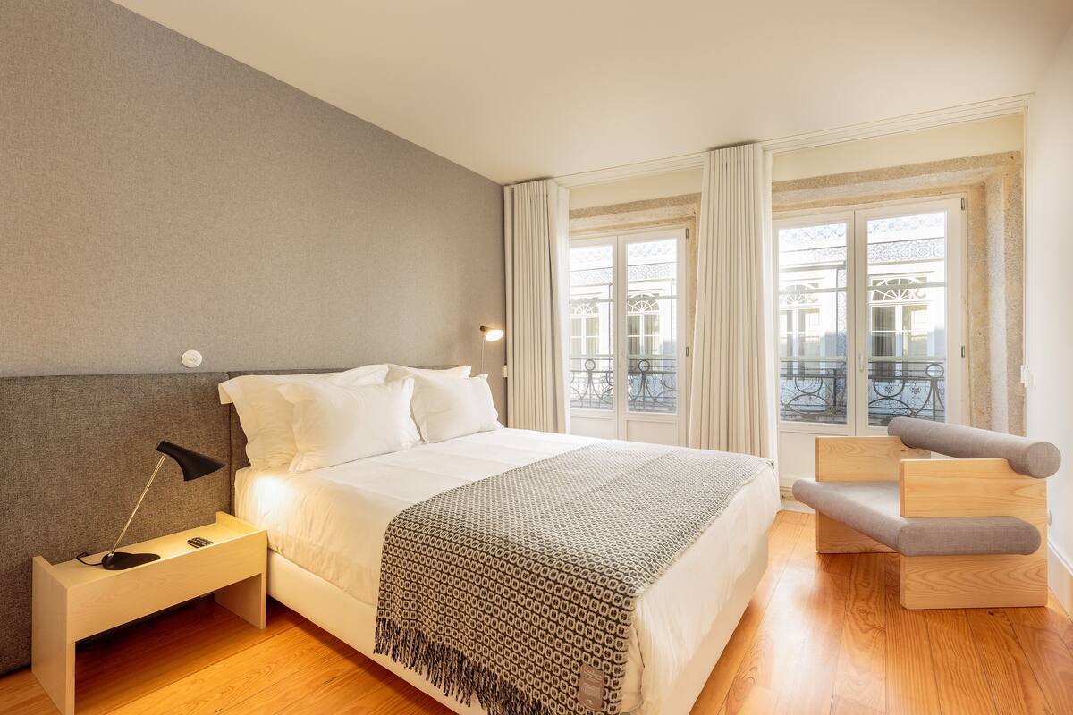 A bedroom with a bed, bedside table, lamp, and a chair.