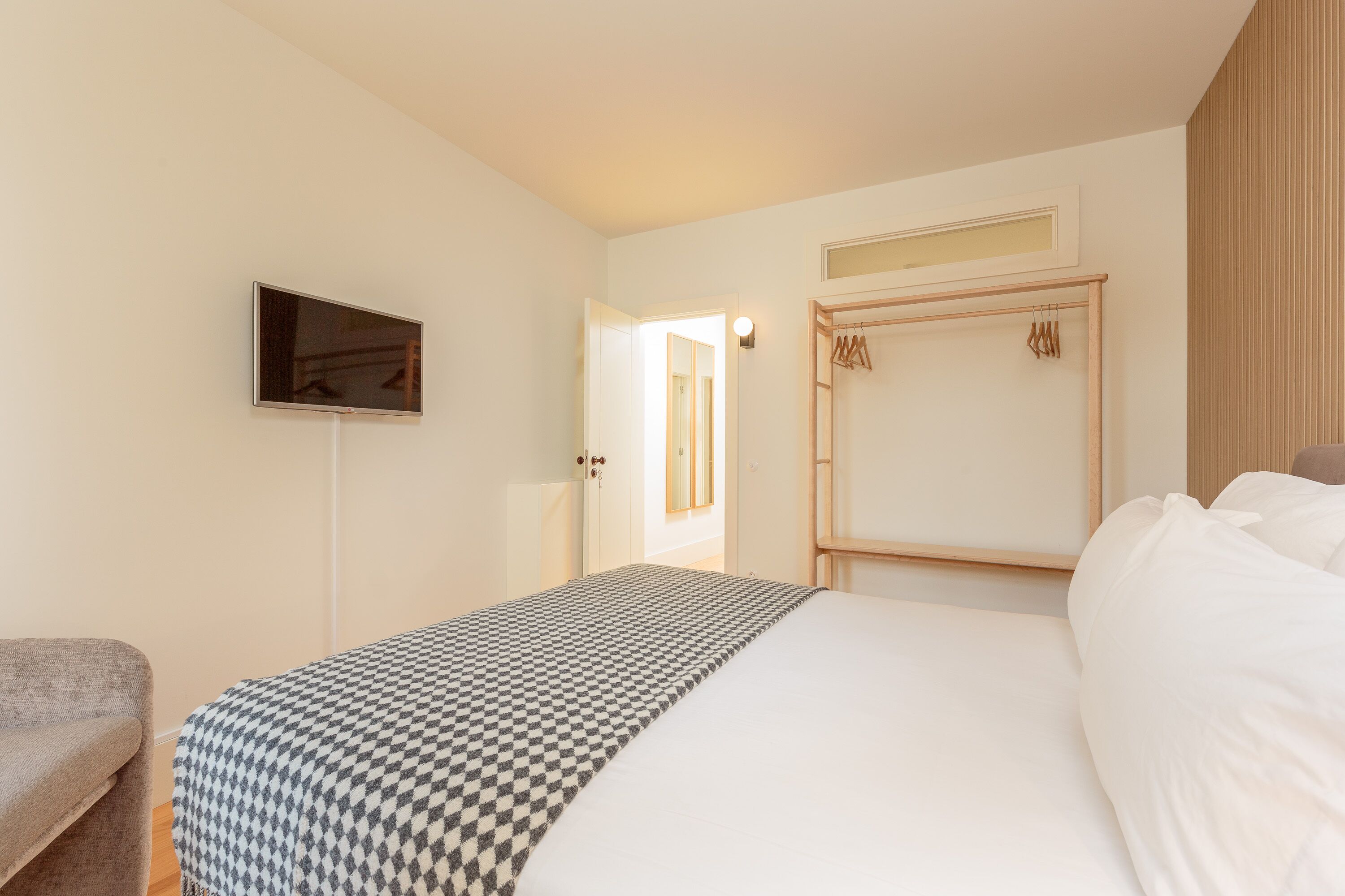 Una habitación de hotel con cama, televisión, armario y una puerta que da a otra habitación.