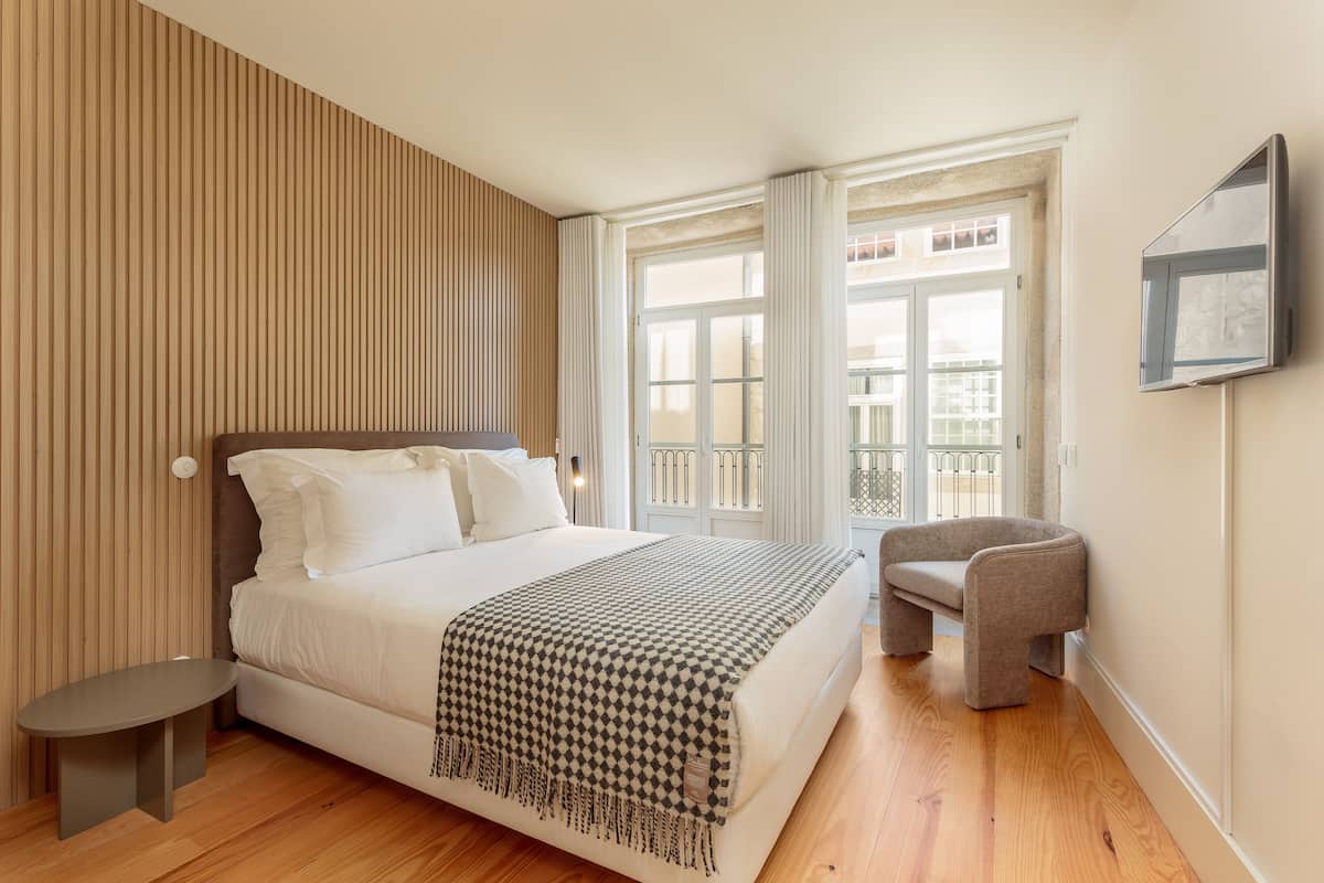 A bedroom with a bed, bedside table, chair, and a TV mounted on the wall.