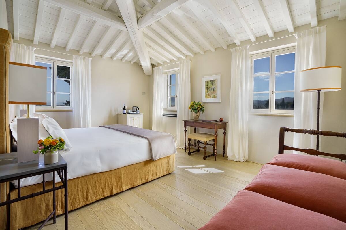 A bedroom with a bed, a desk, a chair, a lamp, and a window with curtains.