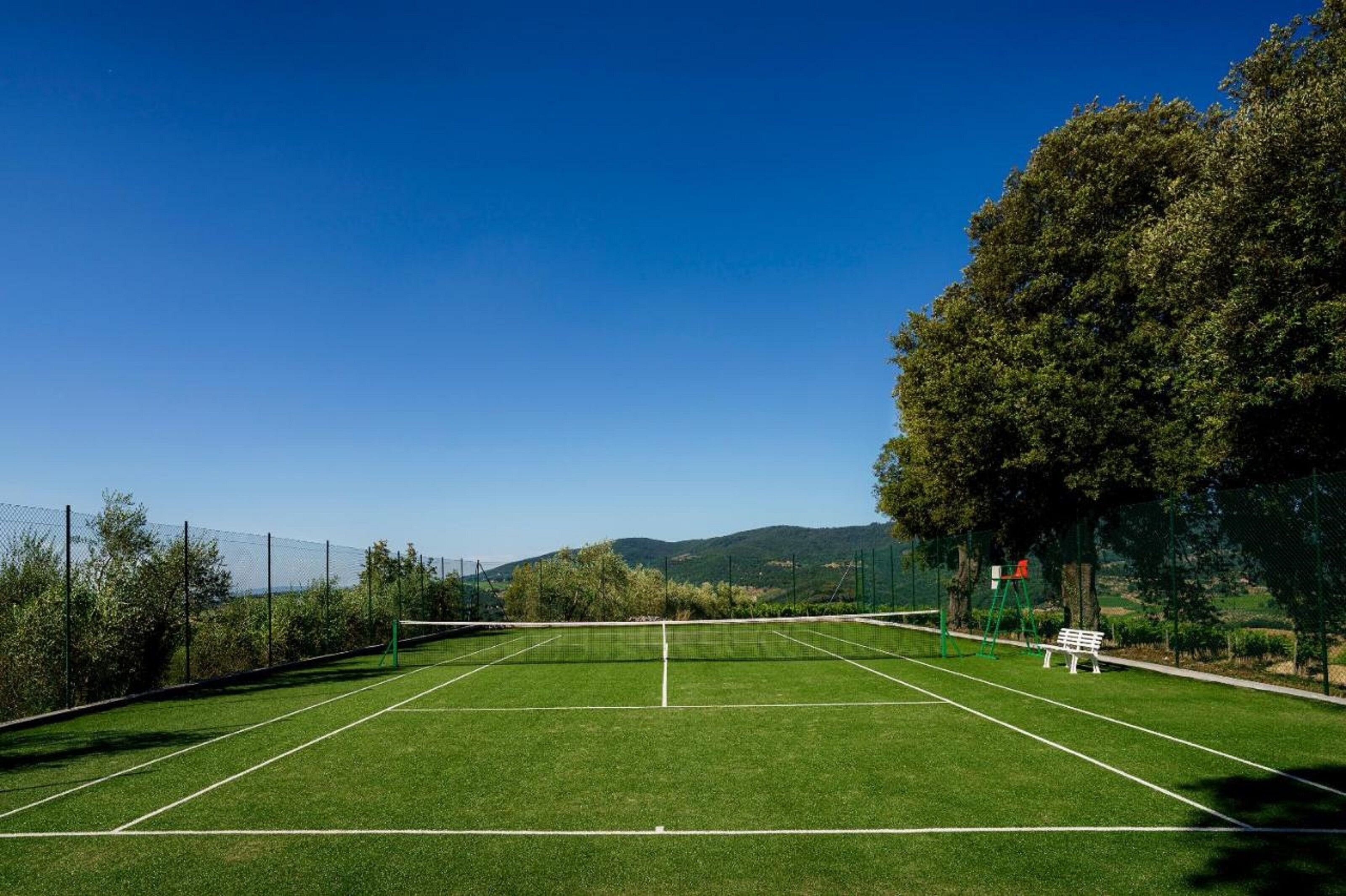 Un court de tennis avec un filet, entouré d’arbres et agrémenté d’un banc.