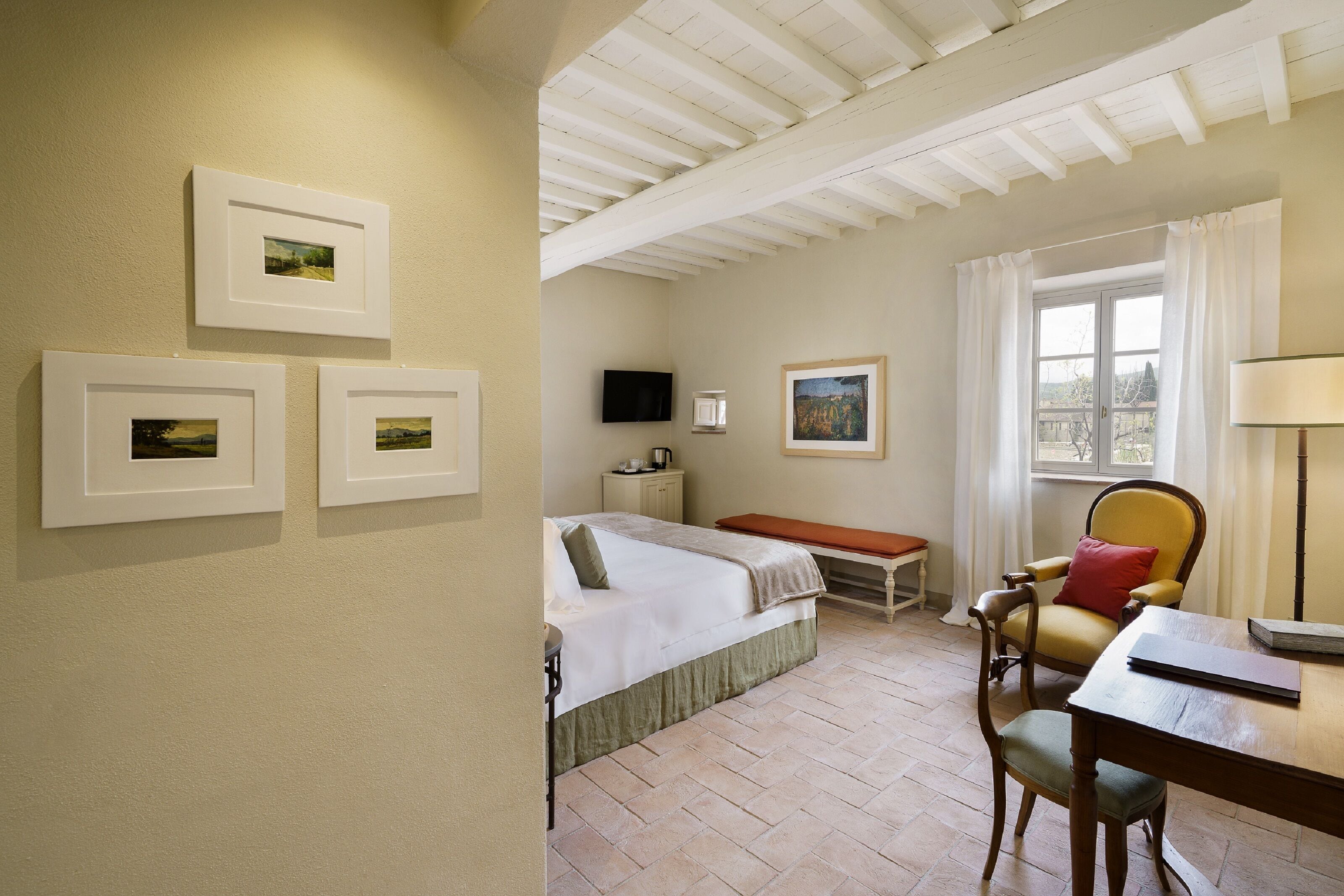 A room with a bed, a chair, a table, and artwork on the walls.