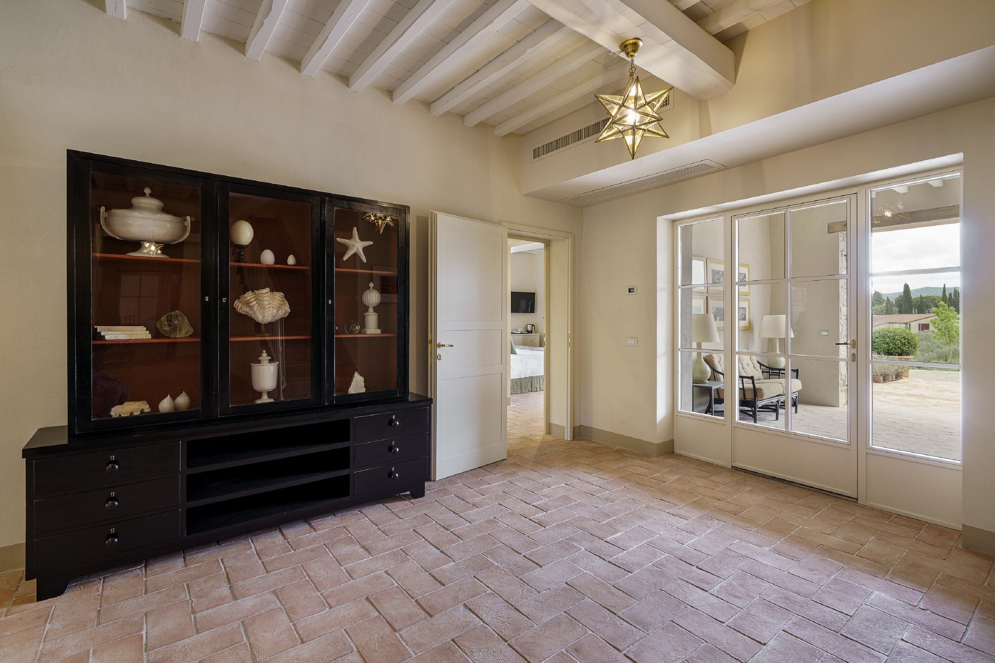 Ein Zimmer mit einem dunklen Holzschrank mit Glastüren, einem gefliesten Boden und einem großen Fenster mit Blick ins Freie.
