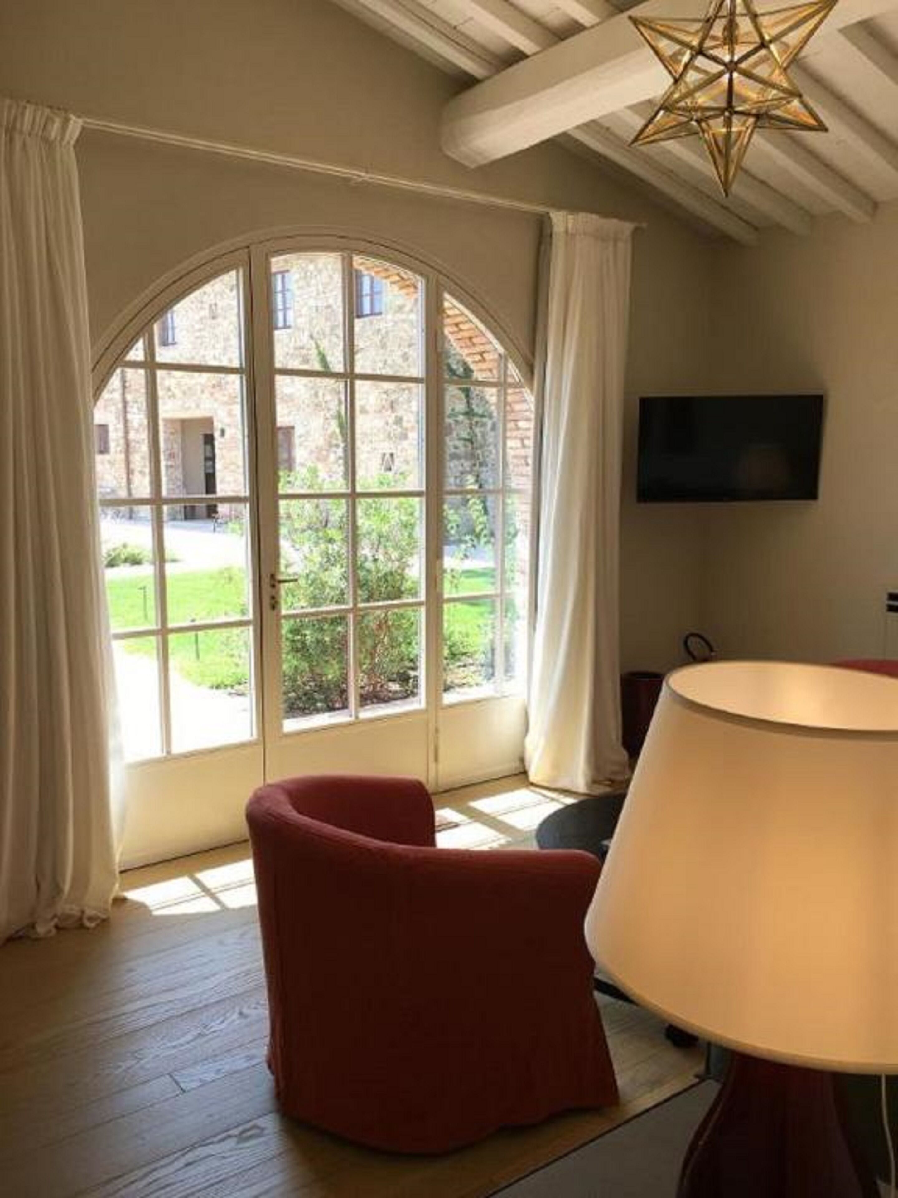 A room with a large arched window, a red chair, a table with a lamp, and a flat-screen TV mounted on the wall.
