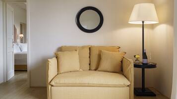 A beige sofa with multiple cushions, a round mirror on the wall, a floor lamp, and a small table with a bottle and glass.