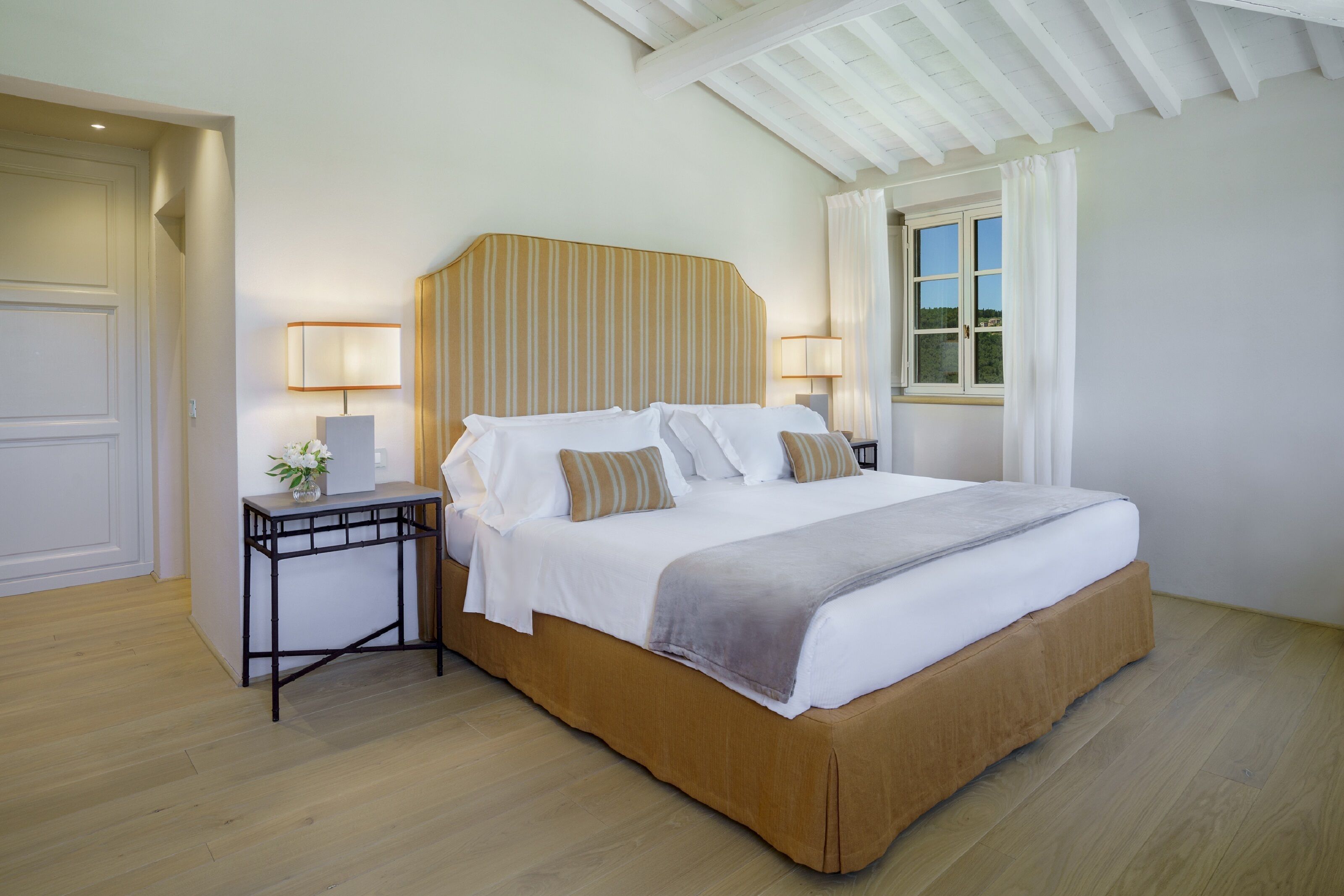 Un dormitorio ordenado con una cama grande, lámparas de noche y una ventana con cortinas.