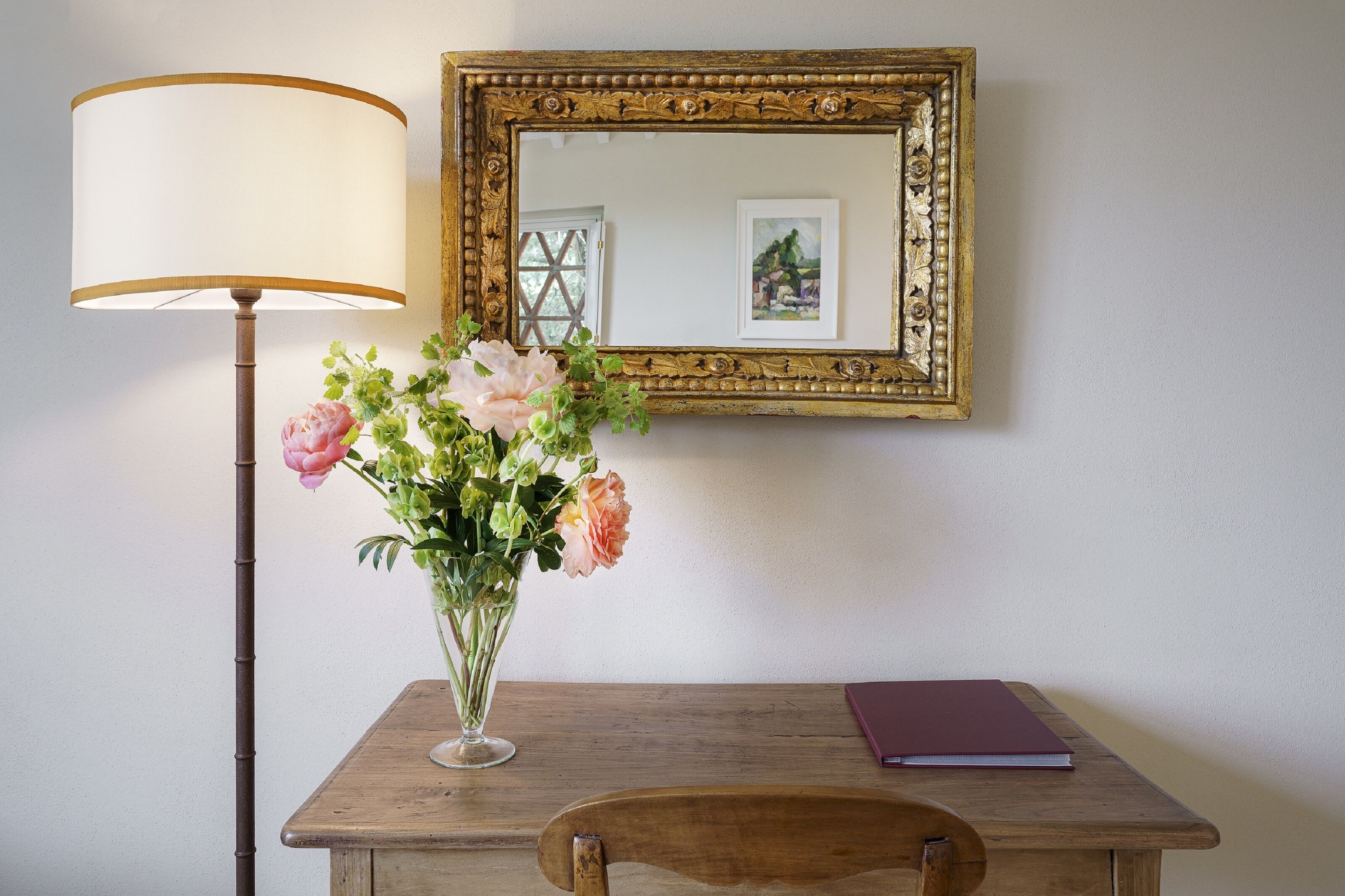 Ein Holztisch mit Blumen in einer Vase, einer Lampe und einem gerahmten Bild an der Wand.