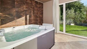 A modern bathroom with a large bathtub, marble tiles, and a sliding glass door leading to a garden. - Charming Villa Grgo with a pool and a mini wellness (Tinjan)