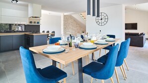 A modern dining area with a long table set for six, blue upholstered chairs, and a kitchen in the background. - Elegant Villa Dolcea with a swimming pool (Kaštel)