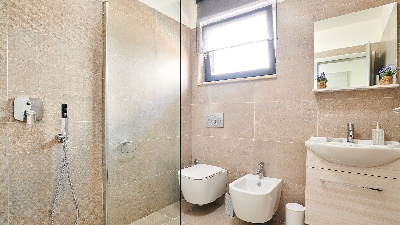 Ein modernes Badezimmer mit Duschkabine aus Glas, Toilette, Bidet und Waschbecken mit Spiegel darüber.