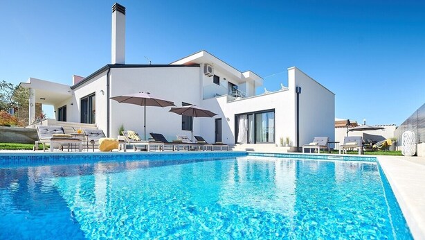 A modern house with a swimming pool, lounge chairs, and umbrellas. - Elegant Villa Dolcea with a swimming pool (Kaštel)