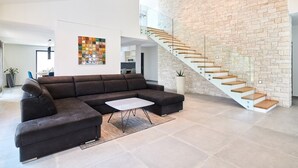 A modern living room with a sectional sofa, a glass staircase, and a brick wall. - Elegant Villa Dolcea with a swimming pool (Kaštel)