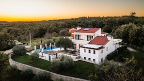 Ein modernes, zweistöckiges Haus mit Swimmingpool, umgeben von üppiger Vegetation und einer Steinmauer.