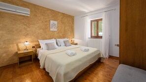 A neatly arranged bedroom with a wooden floor, a bed with white linens, two bedside tables with lamps, a window with curtains, and a radiator. - Stone villa Zamask with a pool and a lovely view (Pazin)