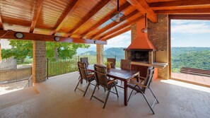An outdoor patio with a stone fireplace, wooden ceiling beams, and a table with chairs. - Stone villa Zamask with a pool and a lovely view (Pazin)